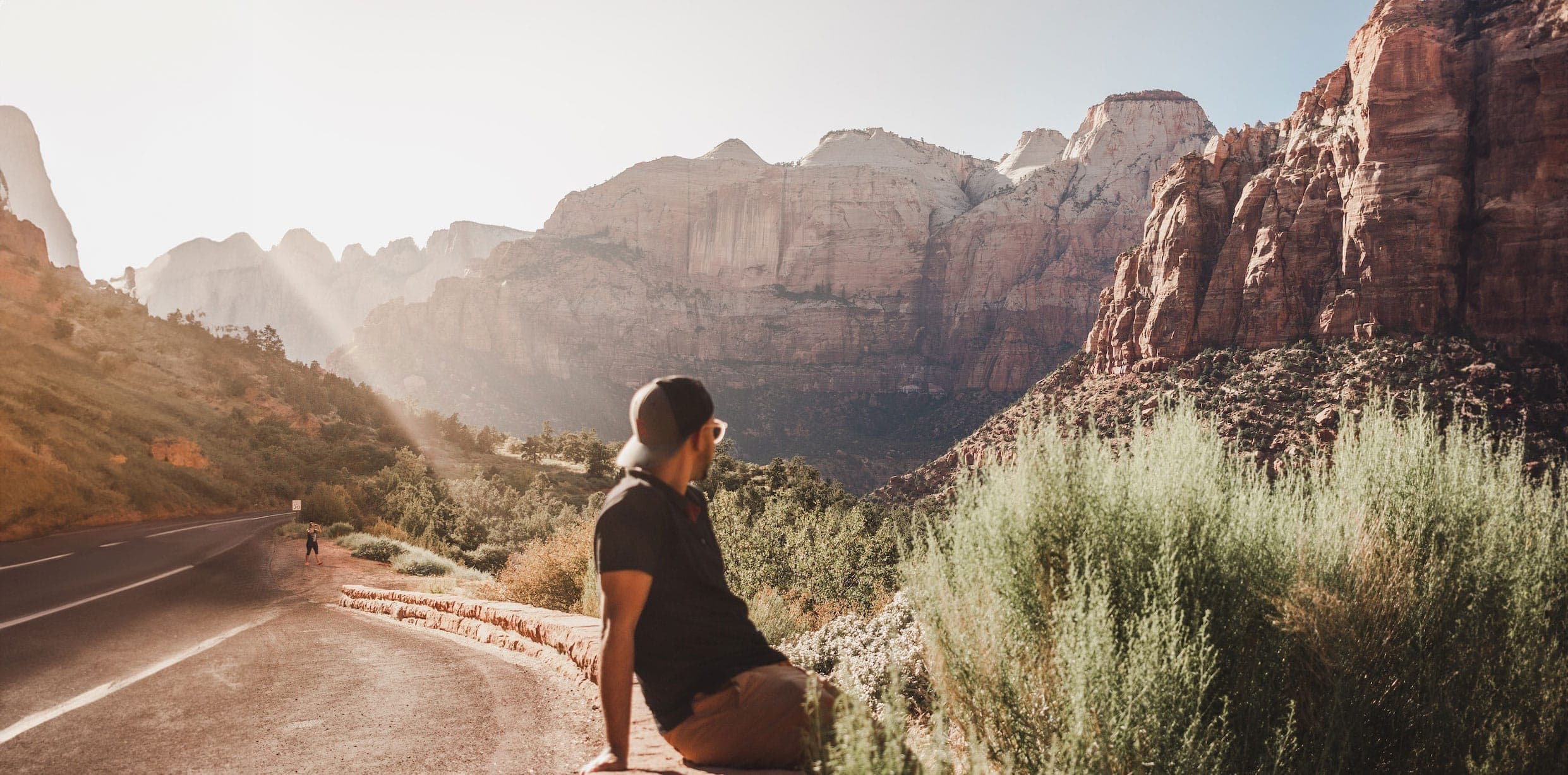 A person sits on a ledge overlooking a vast canyon at sunset.