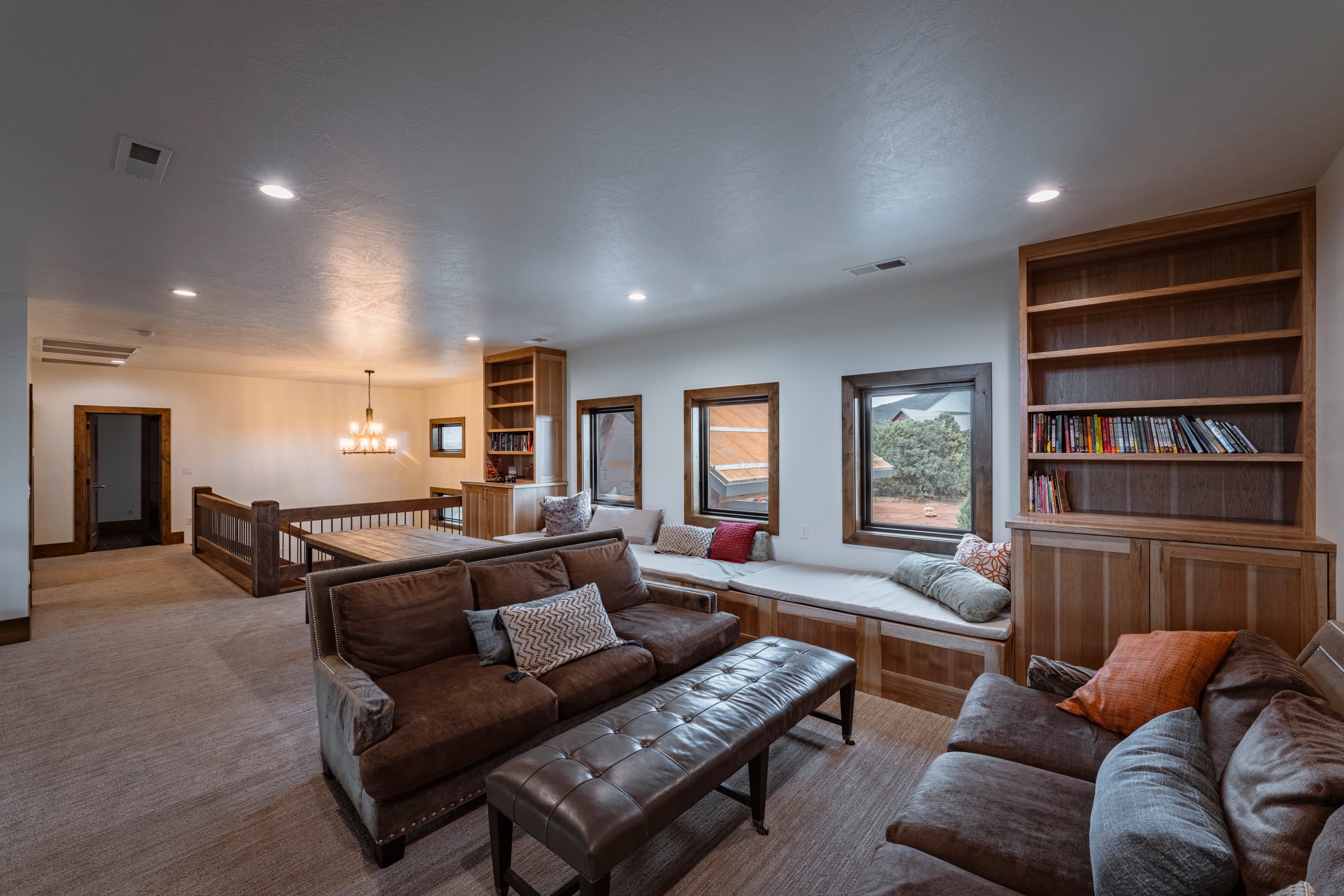 A cozy living area featuring a sectional sofa, benches, and built-in bookshelves with natural light from large windows.