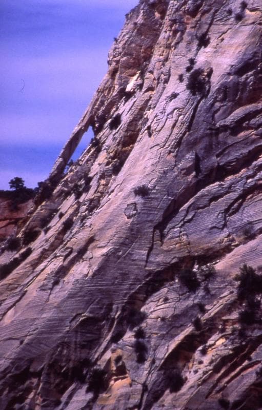 A steep rock formation with layered textures and sparse vegetation.
