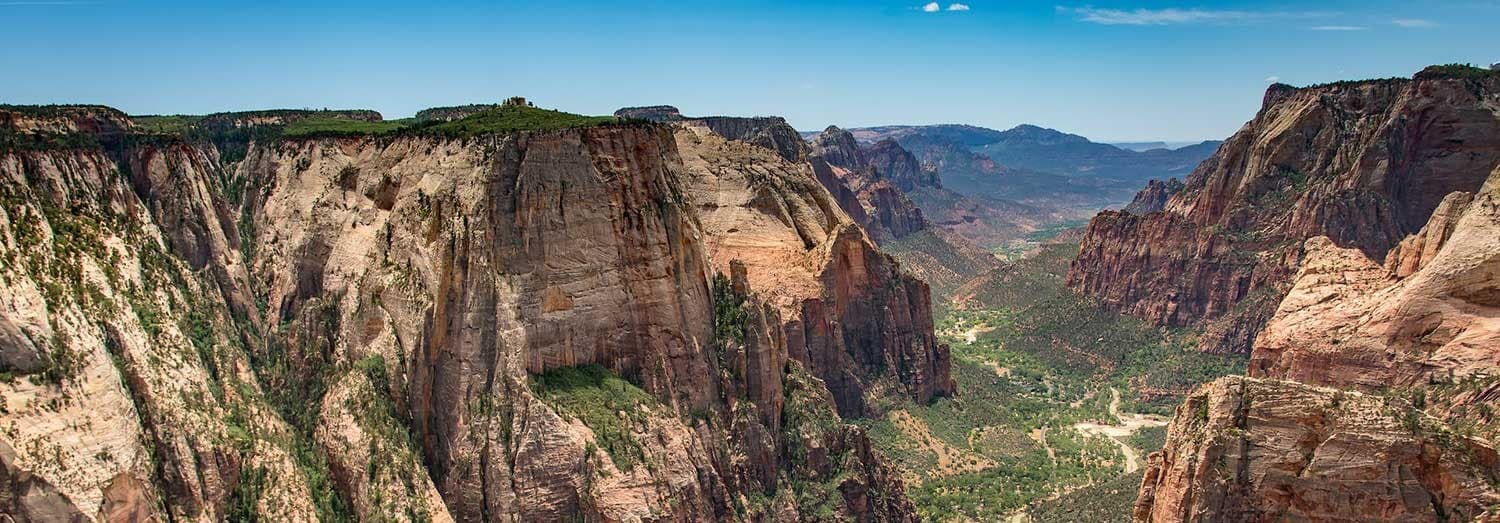 A panoramic view of Zion Canyon featuring steep, colorful cliffs and lush valley below.