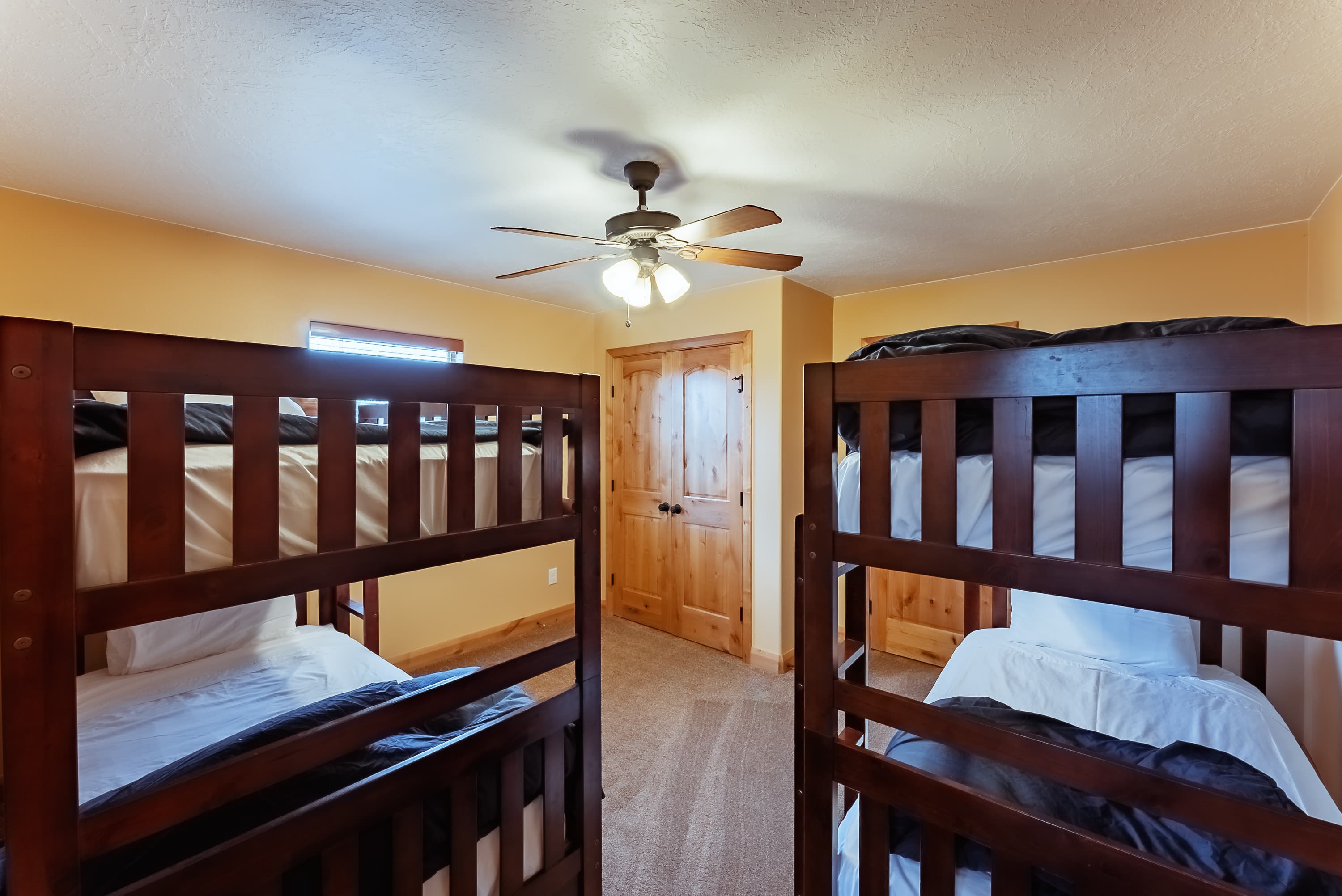 A cozy room featuring two sets of wooden bunk beds and a ceiling fan.