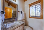 A compact bathroom featuring a sink with a granite countertop, a toilet, and a window with blinds.