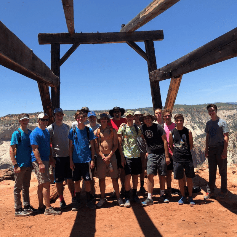 A group of young men poses together under a wooden structure against a clear blue sky.