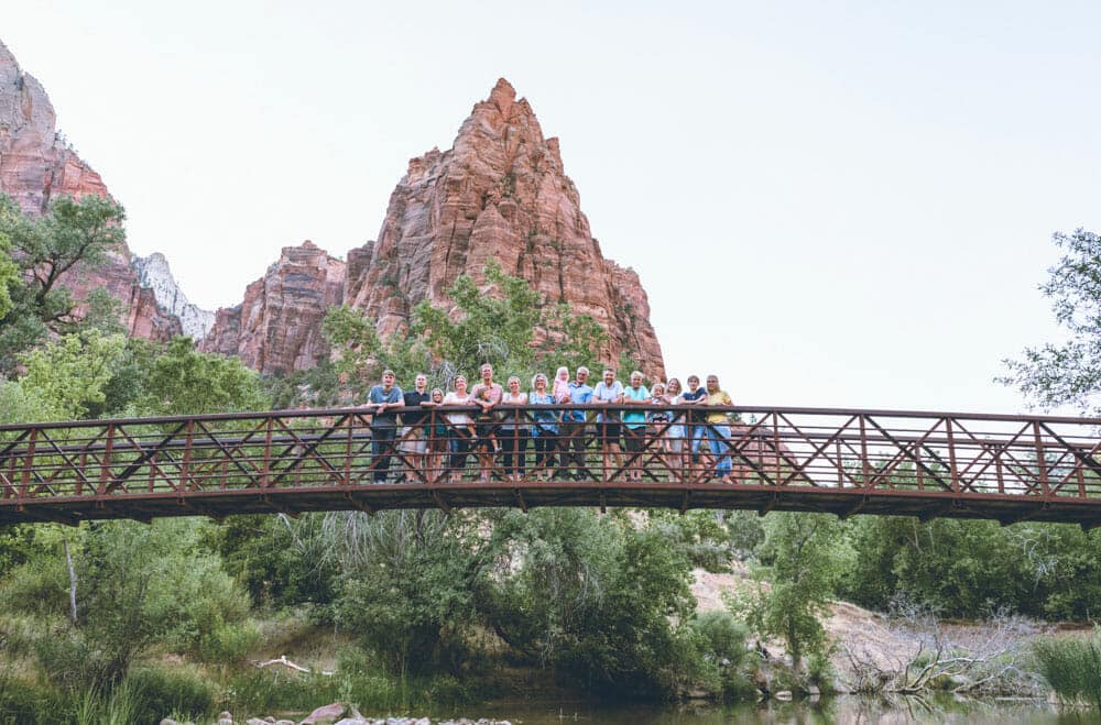 A group of people standing together on a bridge with rocky mountains in the background.