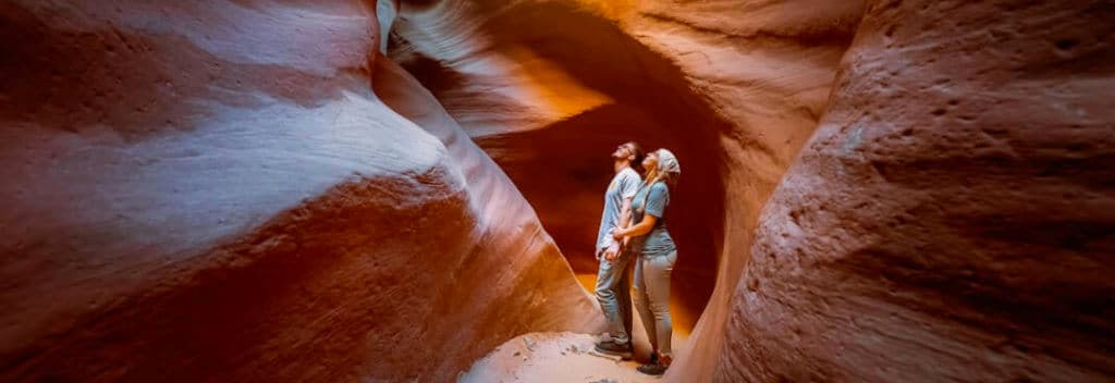 A couple stands together in a stunning sandstone canyon, gazing upwards at the colorful rock formations.