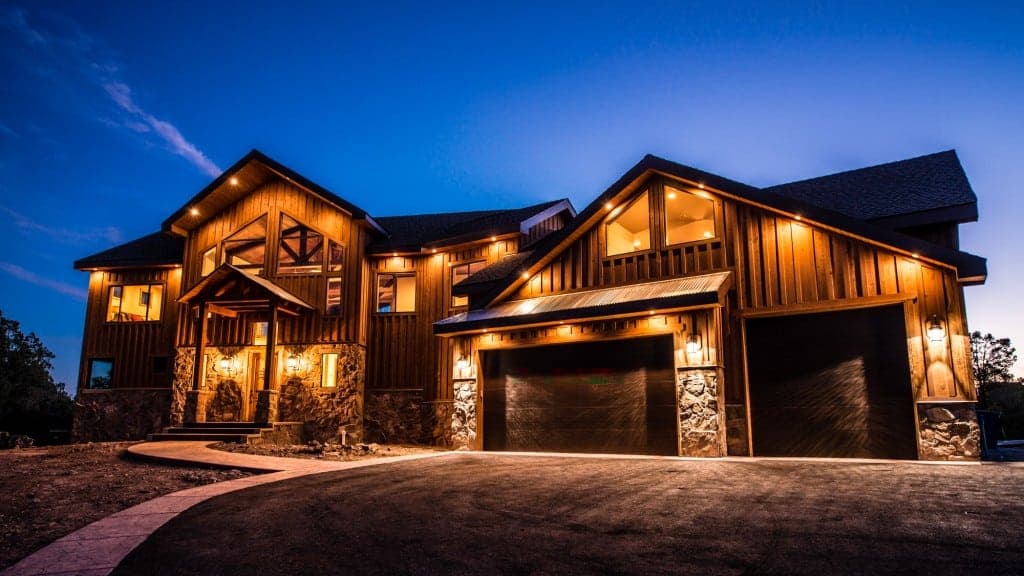 A modern wooden house illuminated at dusk with a curved driveway.