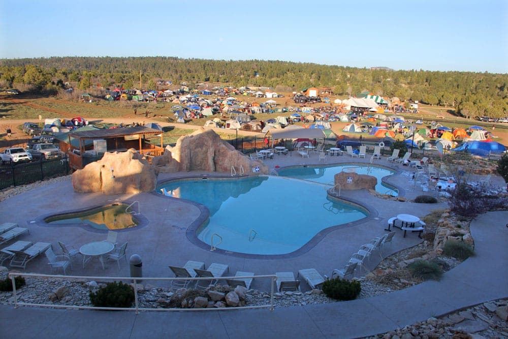 A scenic view of a pool surrounded by lounge chairs and a campground with numerous tents in the background.