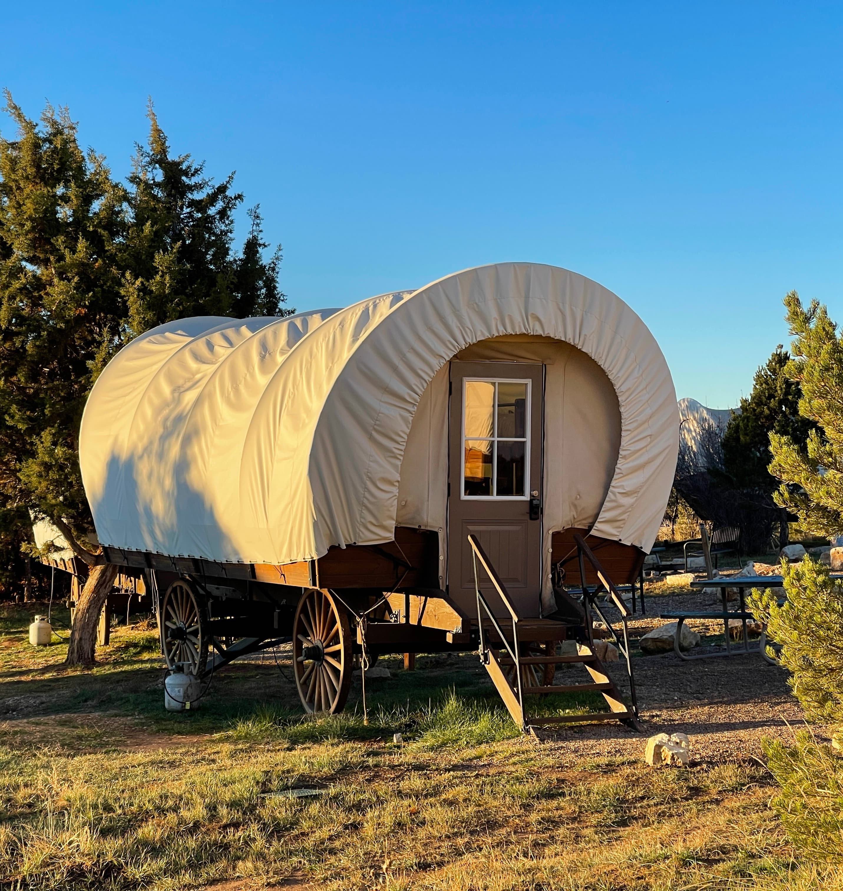 A covered wagon on wheels set against a clear blue sky.