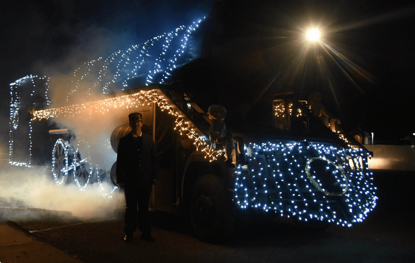 A decorated vehicle wrapped in bright lights and smoke, with a person standing nearby.
