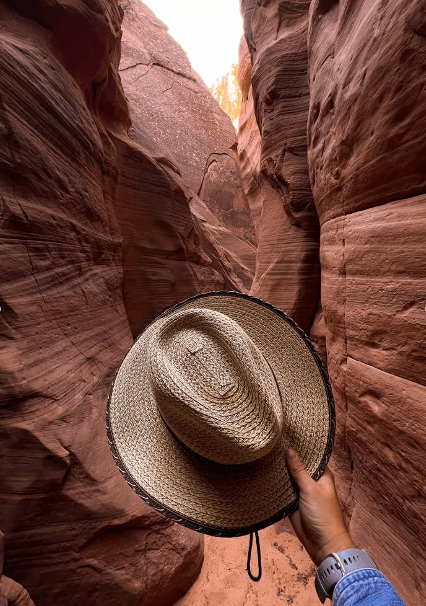 A hand holds a straw hat in a narrow, red canyon.