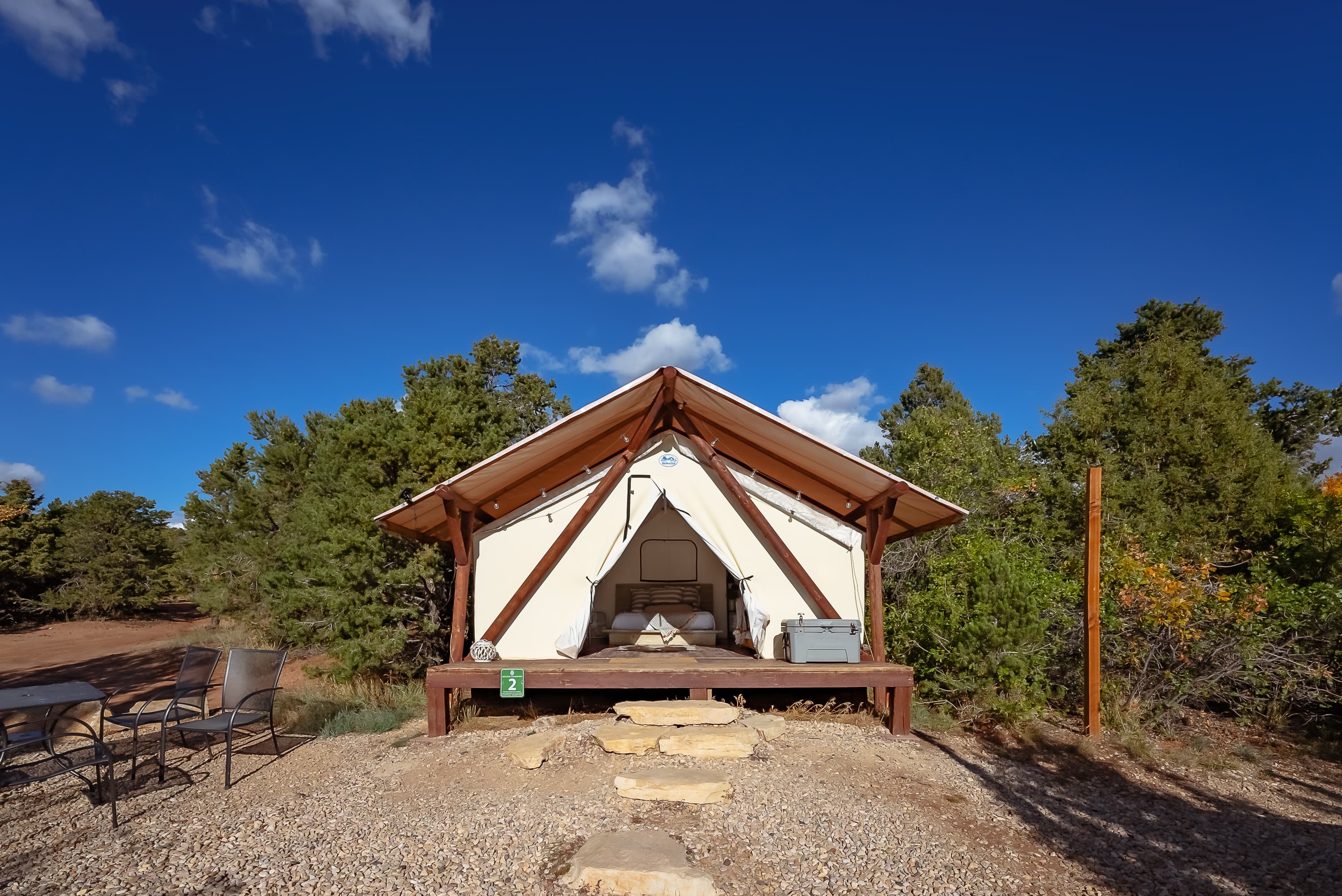 A glamping tent on a wooden platform surrounded by trees and blue skies.