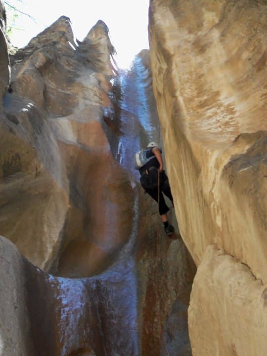 A climber ascends a steep, water-slick rock formation in a canyon.
