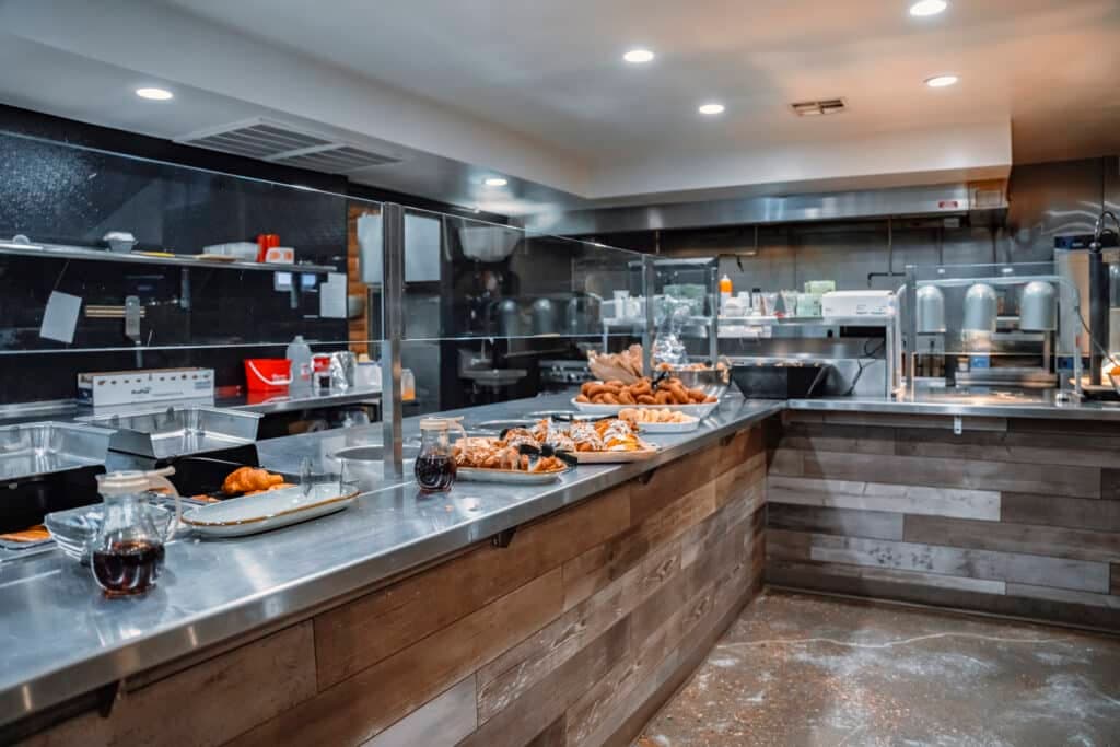 A modern kitchen with stainless steel countertops, various baked goods, and cooking equipment.