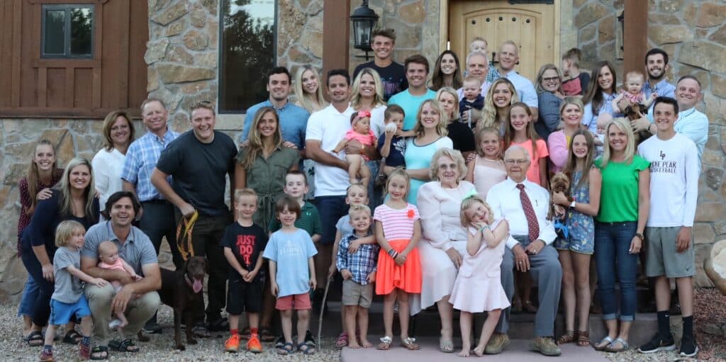 A large family gathers for a group photo on the steps of a stone house.