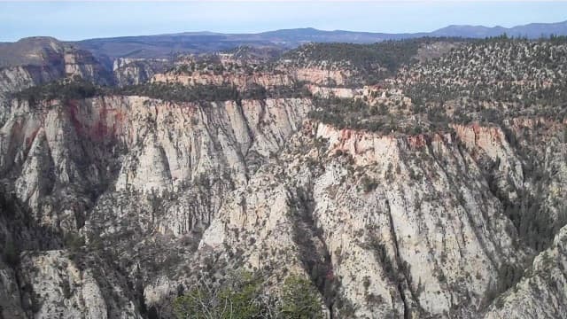 A panoramic view of rugged canyon cliffs and distant mountains under a clear sky.