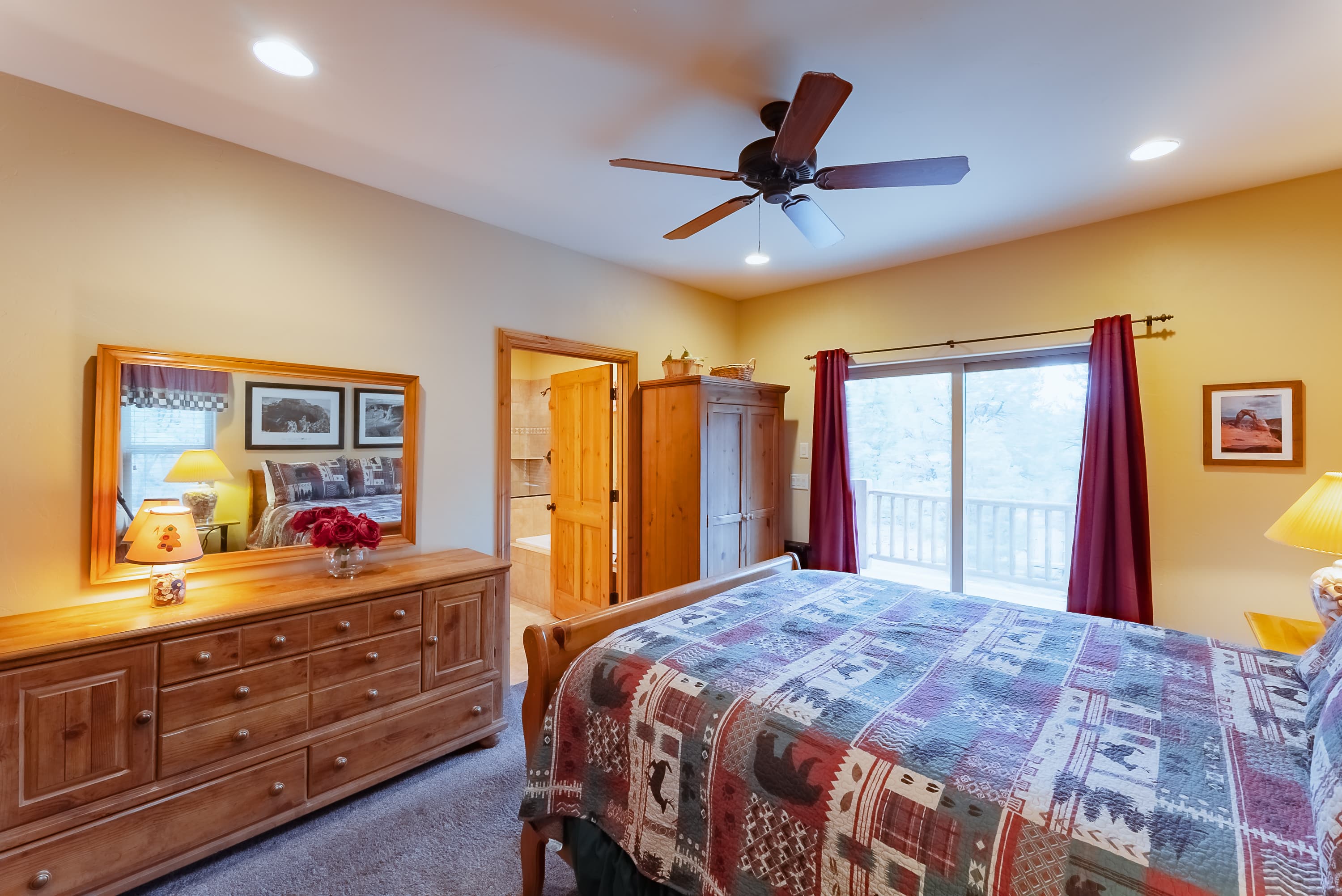Cozy bedroom featuring a wooden dresser, quilted bedspread, and sliding glass door with curtains.