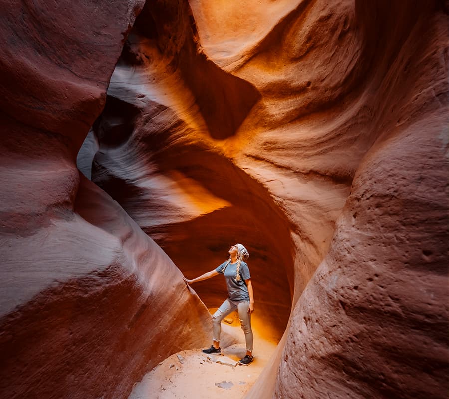 A person stands admiring the swirling red rock formations of a narrow canyon.