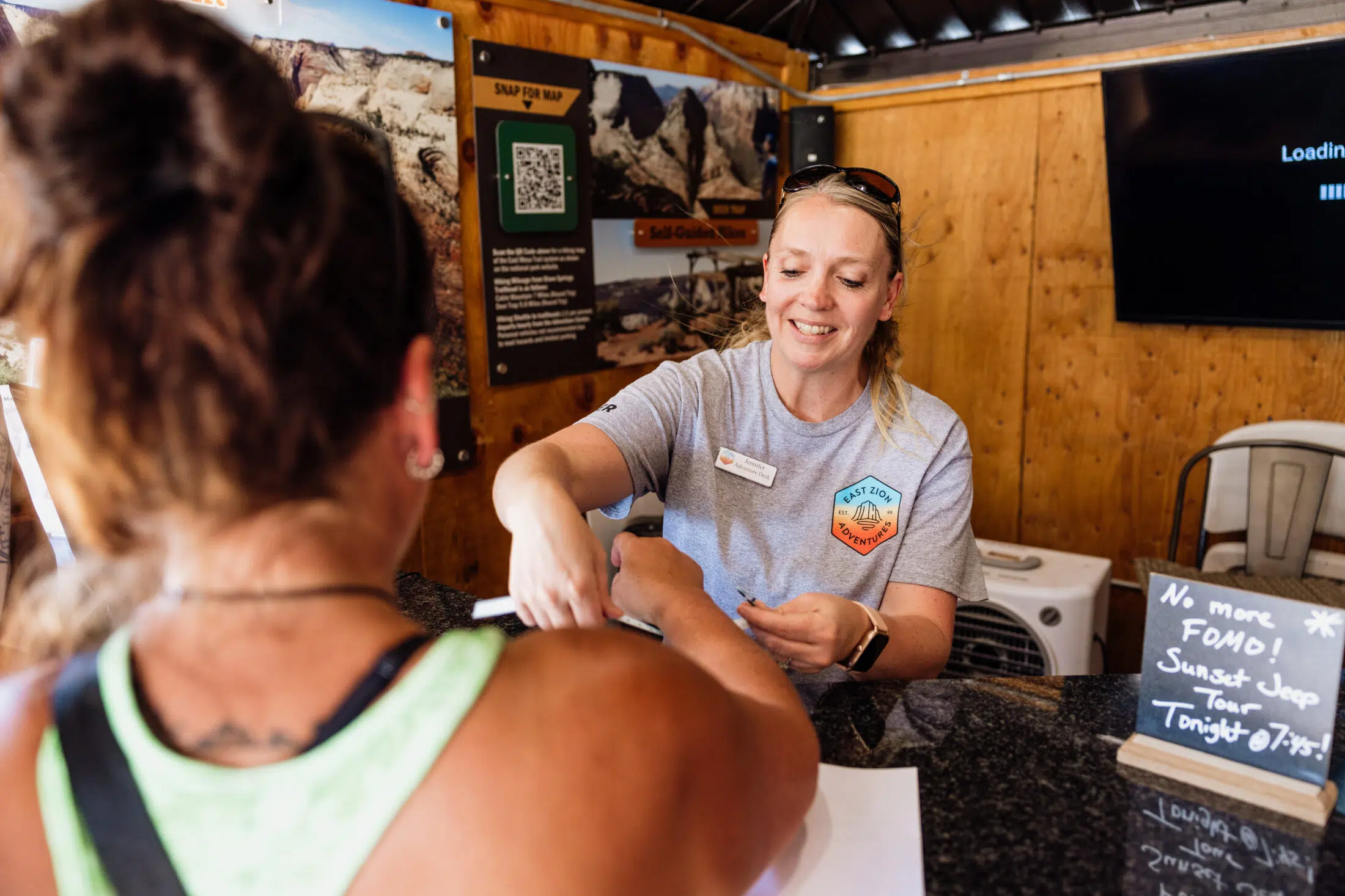 A smiling employee assists a customer at a reception desk in a casual setting.