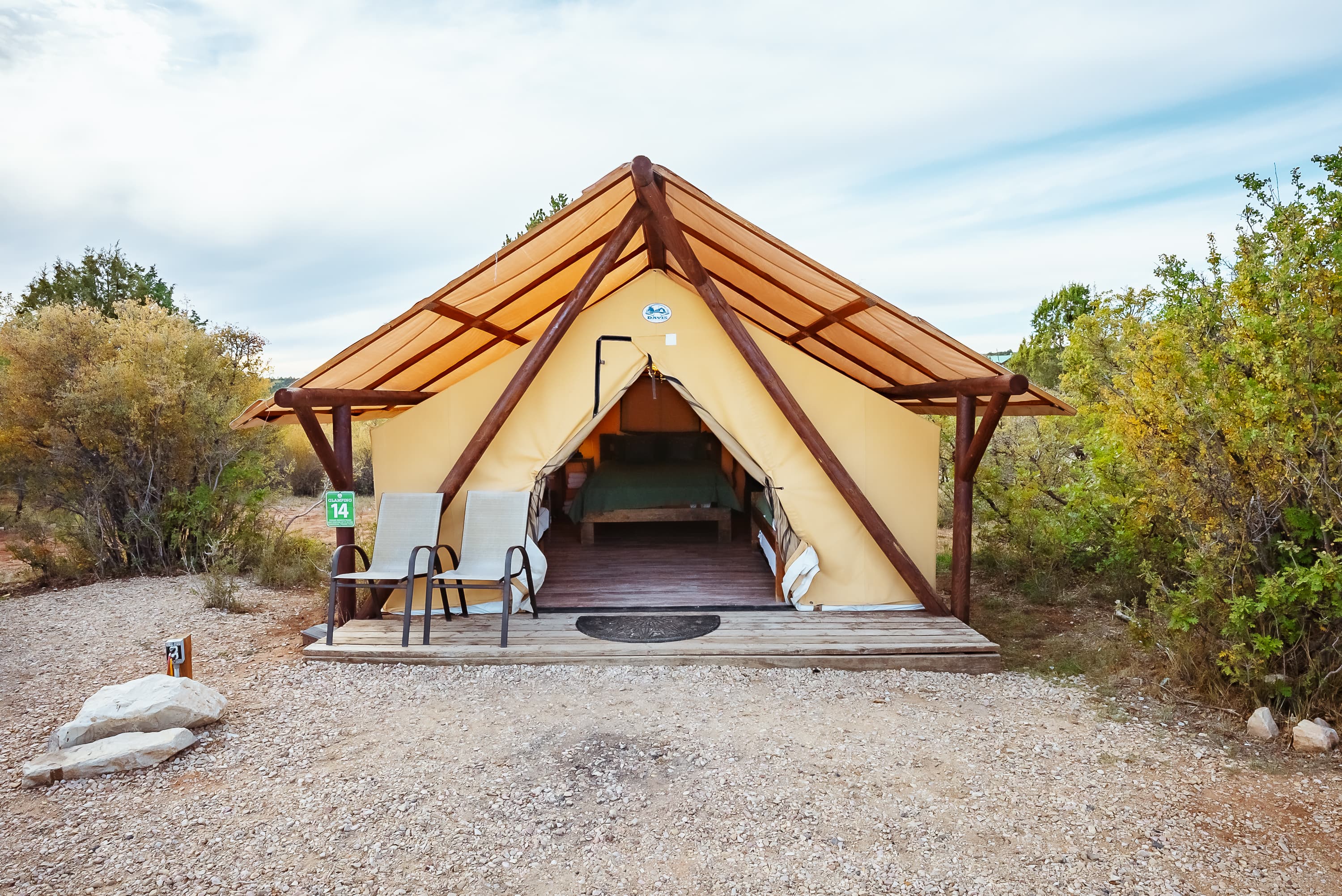 A cozy glamping tent with wooden framing is set in a natural landscape.