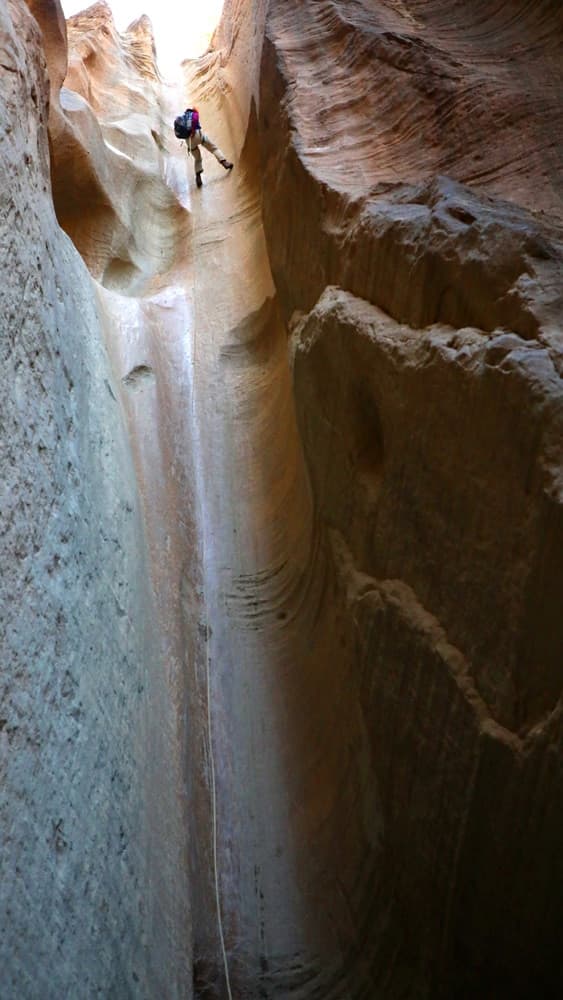 A climber rappels down a narrow, sandstone canyon.