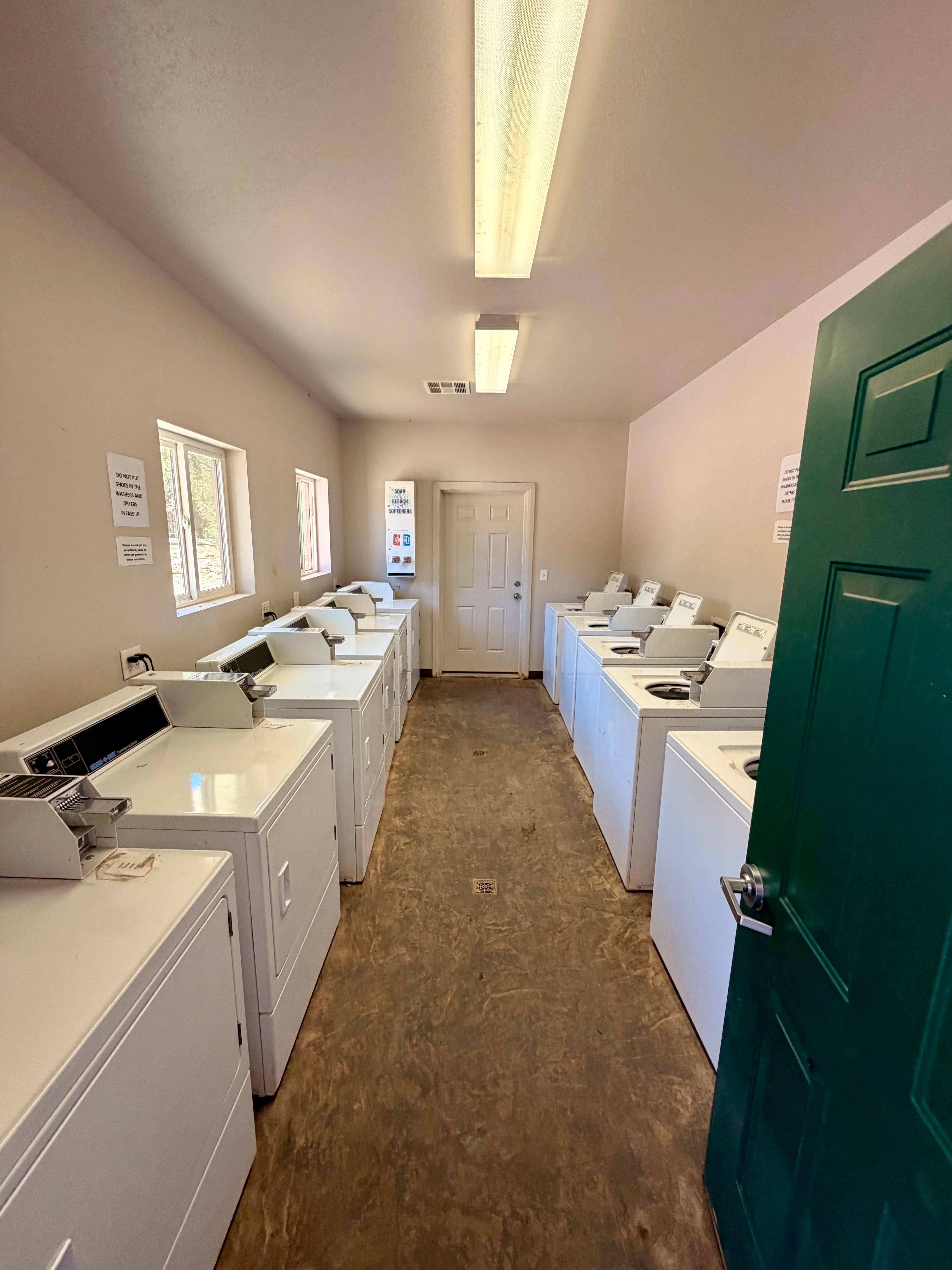 A clean, well-lit laundry room featuring several white washing machines along each side.