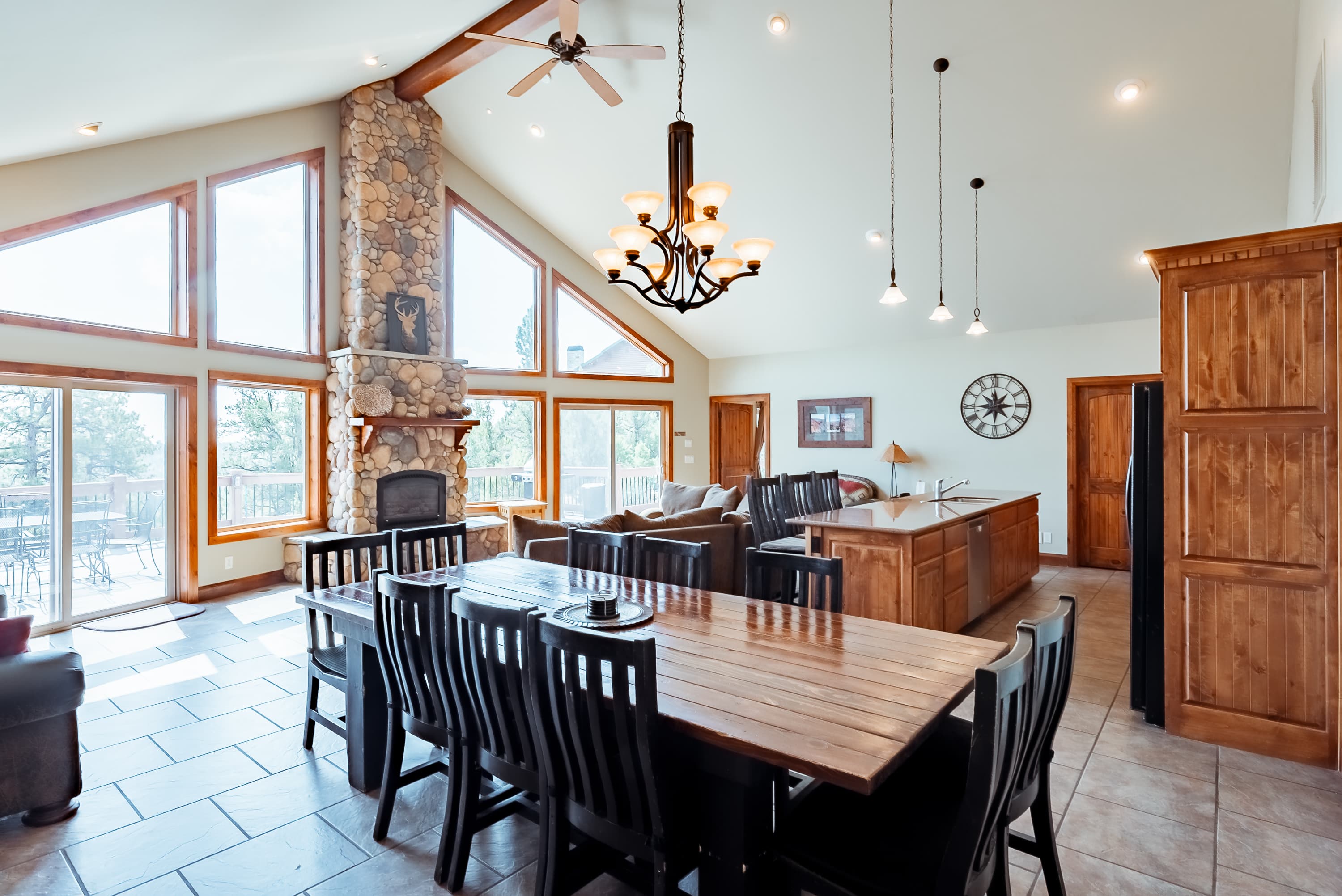 A spacious, modern dining area with a large wooden table, stone fireplace, and large windows.