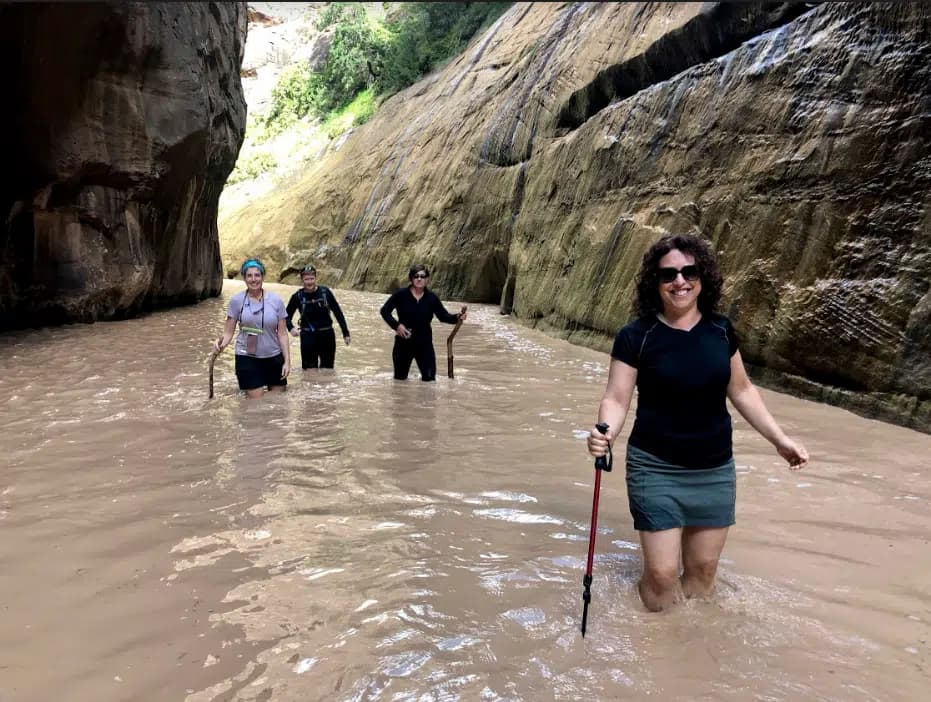 Four people walking through shallow water in a canyon.