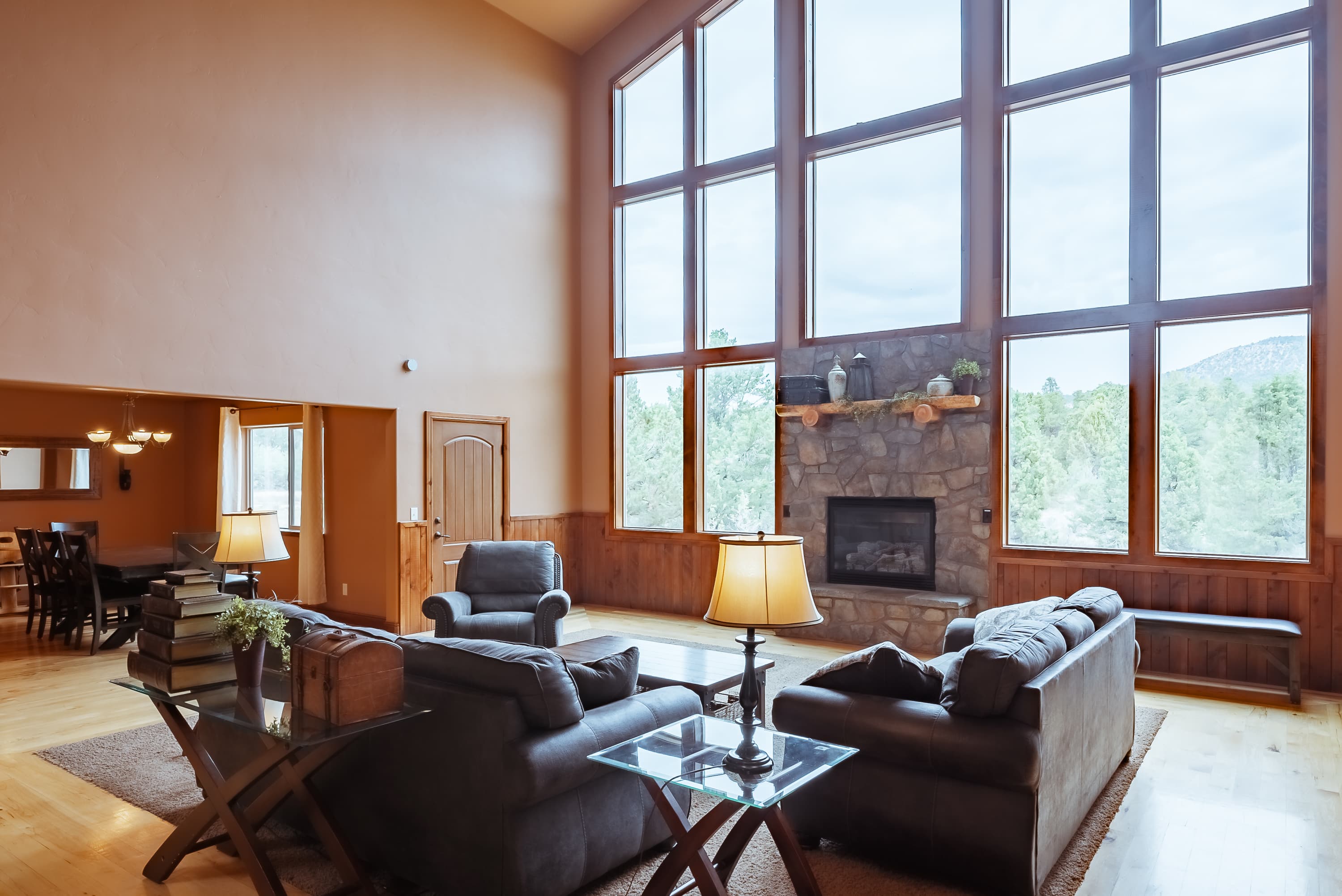A spacious living room with large windows, a stone fireplace, and cozy seating.
