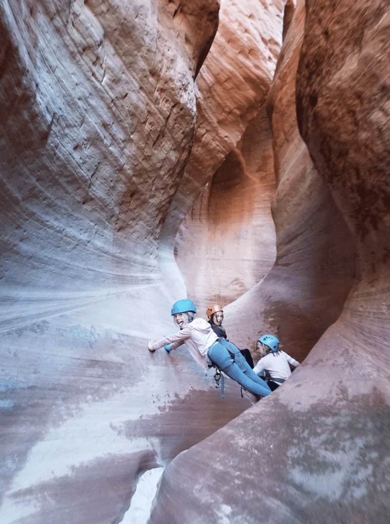 Three climbers navigate a narrow canyon with distinct rock formations.