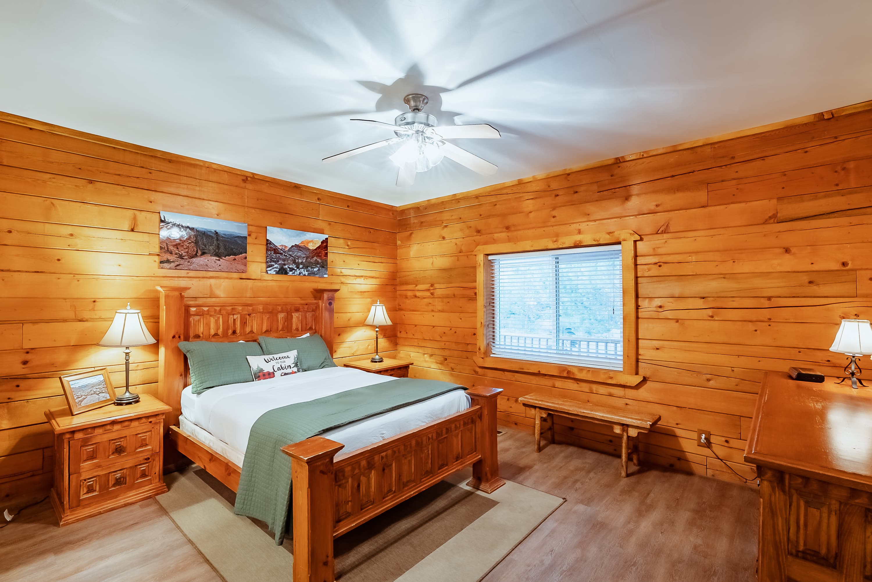 Cozy wooden bedroom featuring a bed, nightstands, a desk, and natural light from a window.