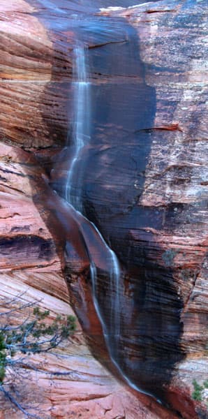 A waterfall cascades down a vibrant red rock face.
