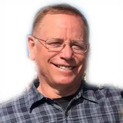 Smiling man wearing glasses and a plaid shirt against a light background.