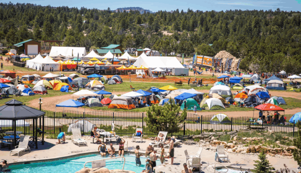 A colorful campsite filled with tents and festival-goers near a swimming pool.