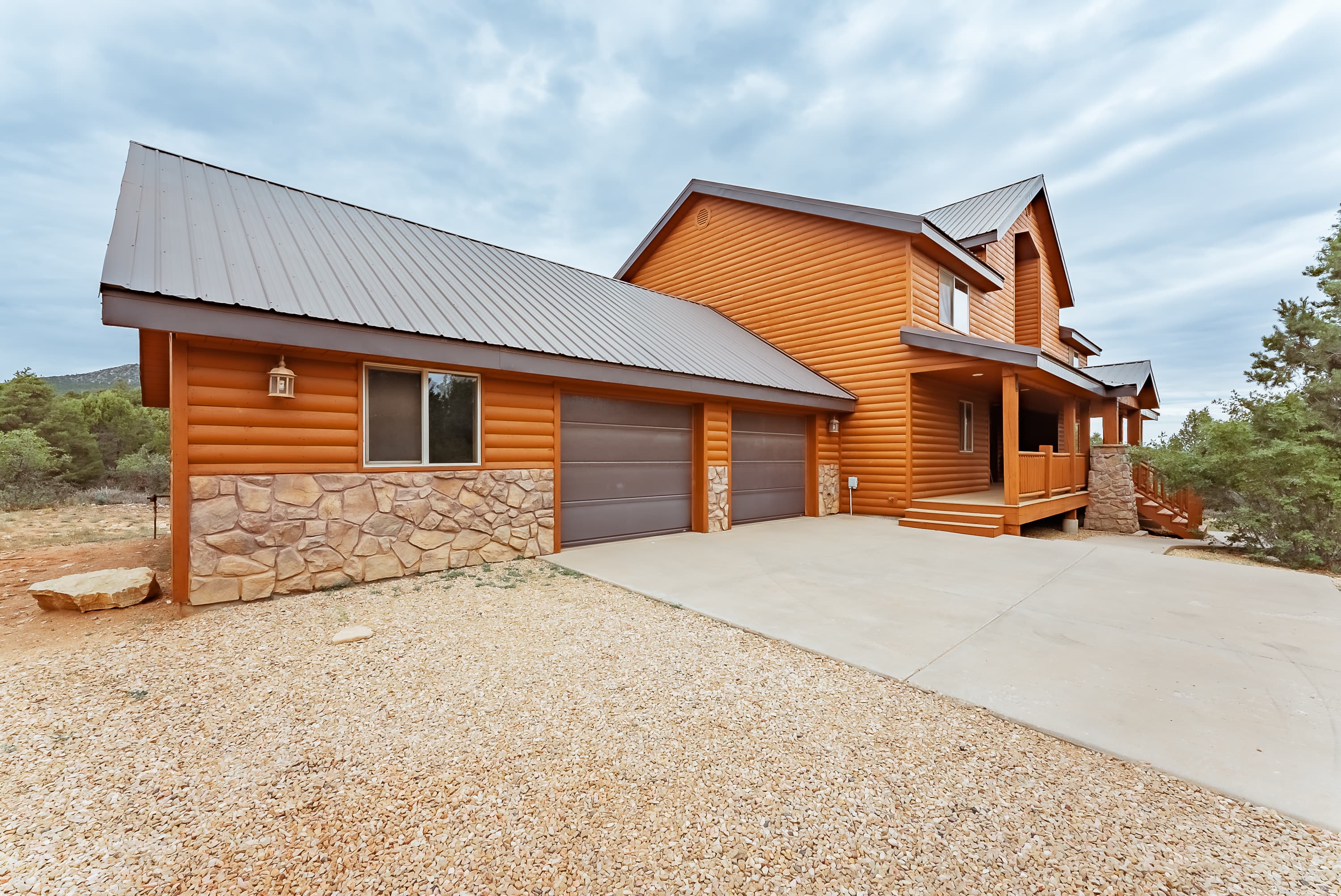 A brown log cabin-style house with a stone facade and garage, set against a cloudy sky.