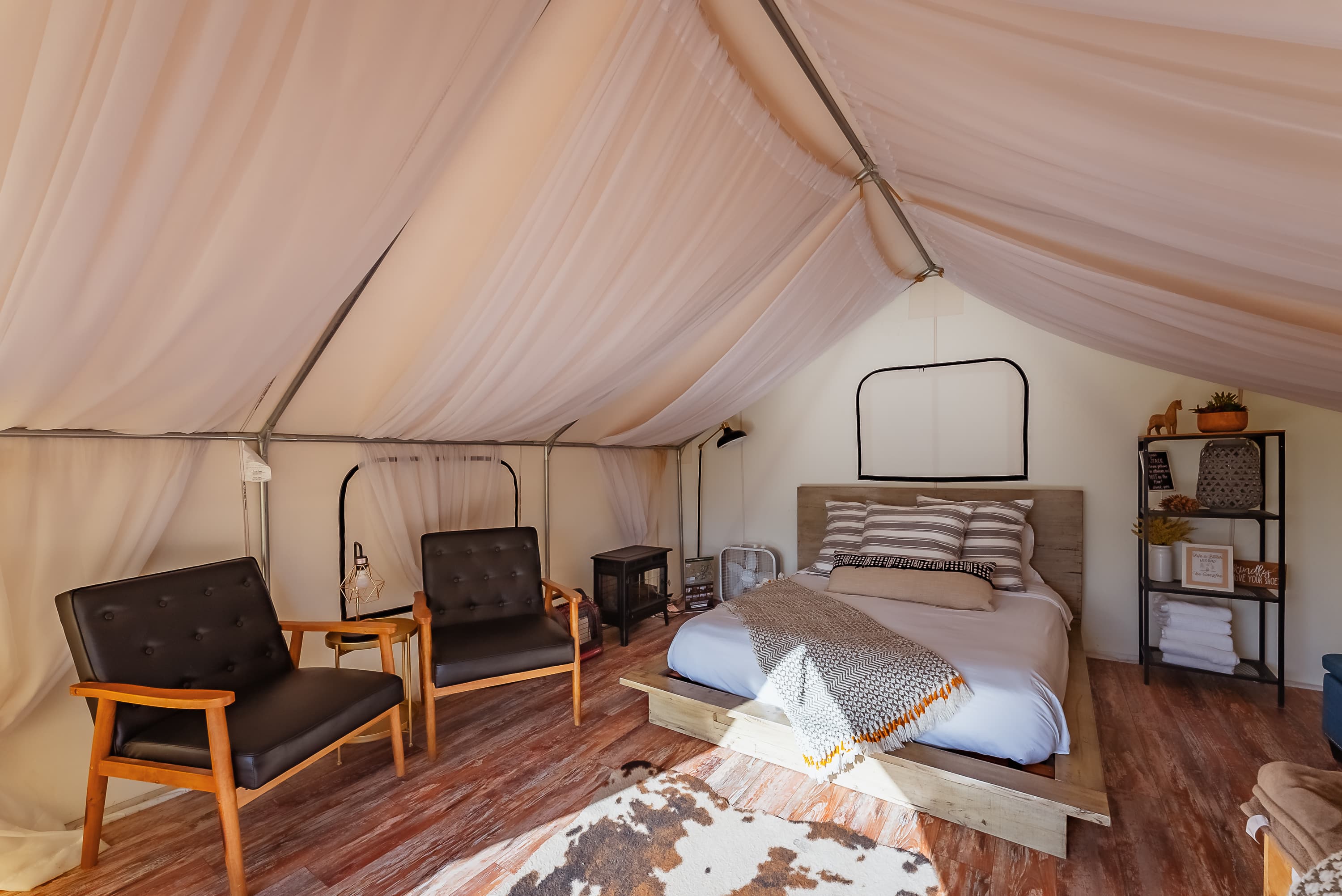 Cozy interior of a tent featuring a bed, two chairs, and wooden flooring.