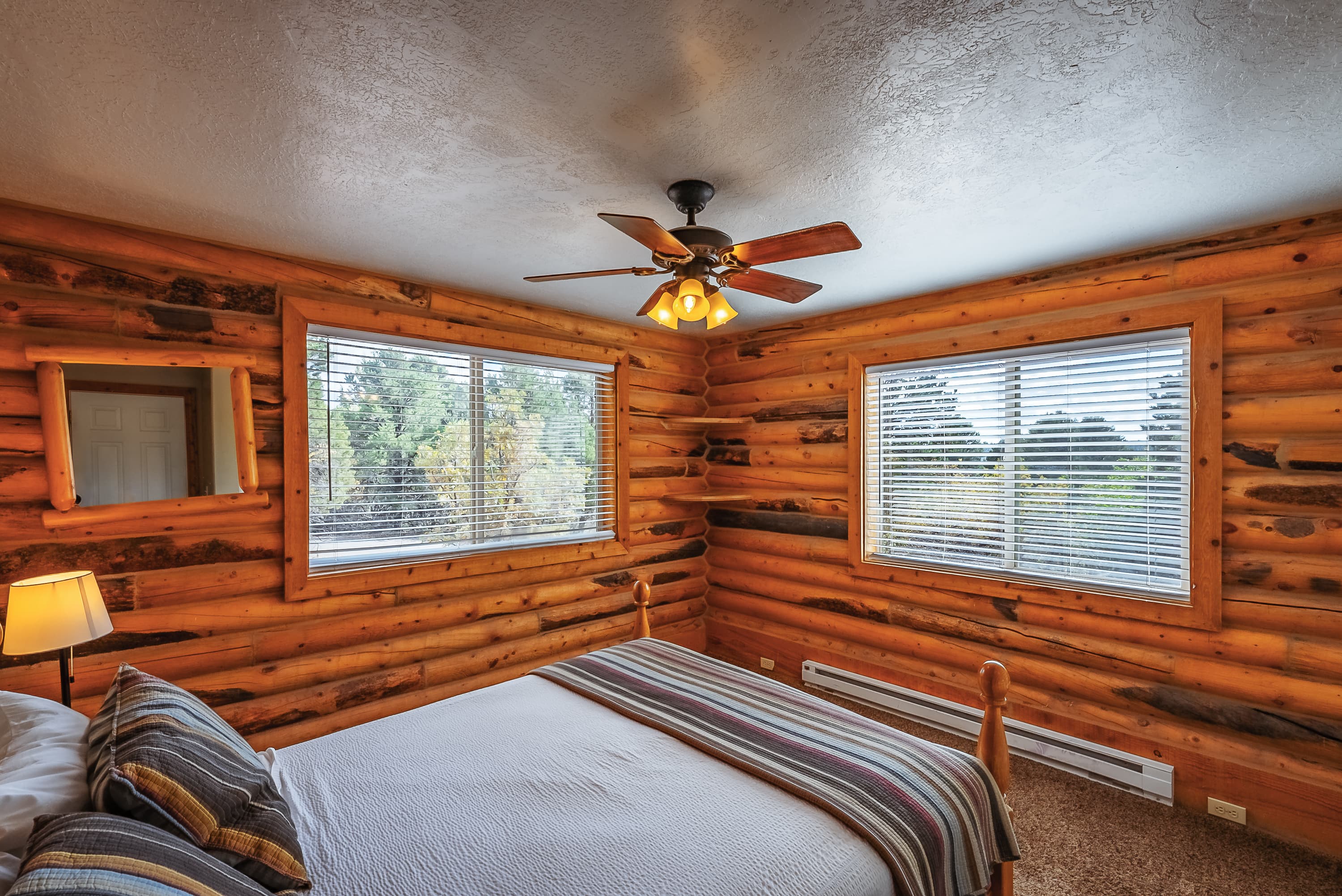 Cozy log cabin bedroom with a bed and large windows featuring nature views.