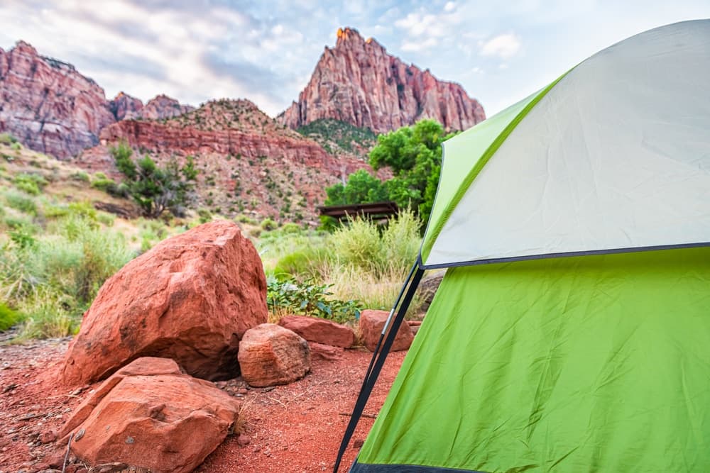 A green tent set against a backdrop of red rock formations and rugged mountains.