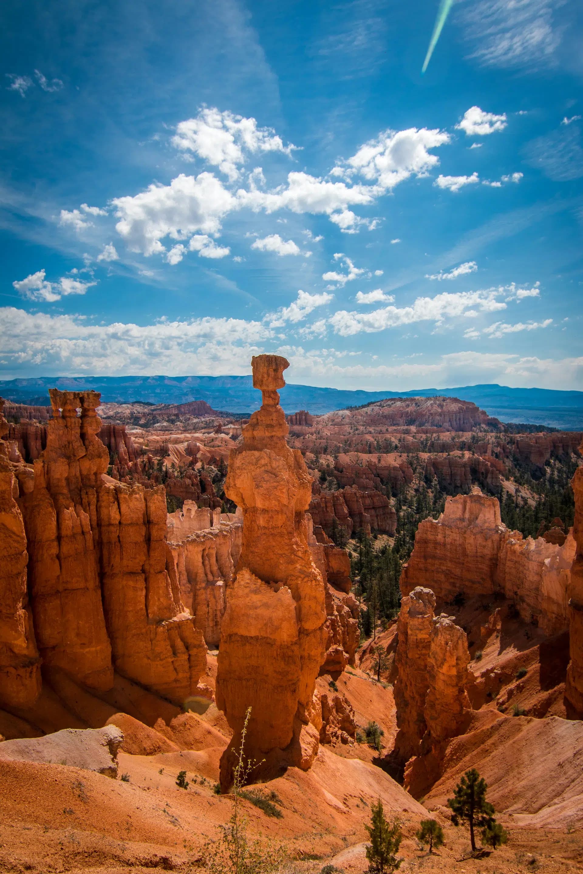 A dramatic landscape featuring towering red rock formations under a bright blue sky with scattered clouds.