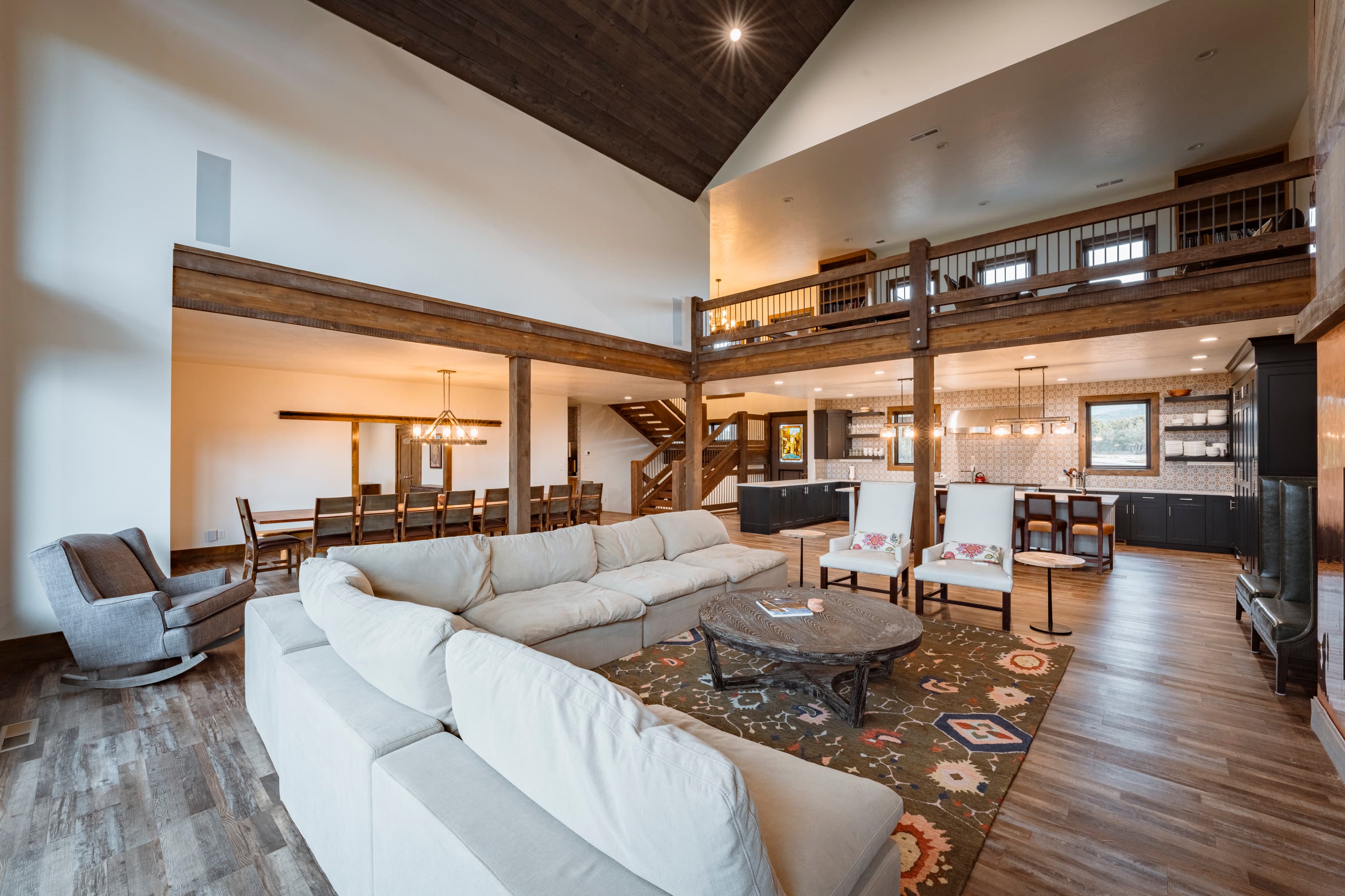 A spacious living area featuring a large sectional sofa, dining space, and an open kitchen with high ceilings and wooden accents.