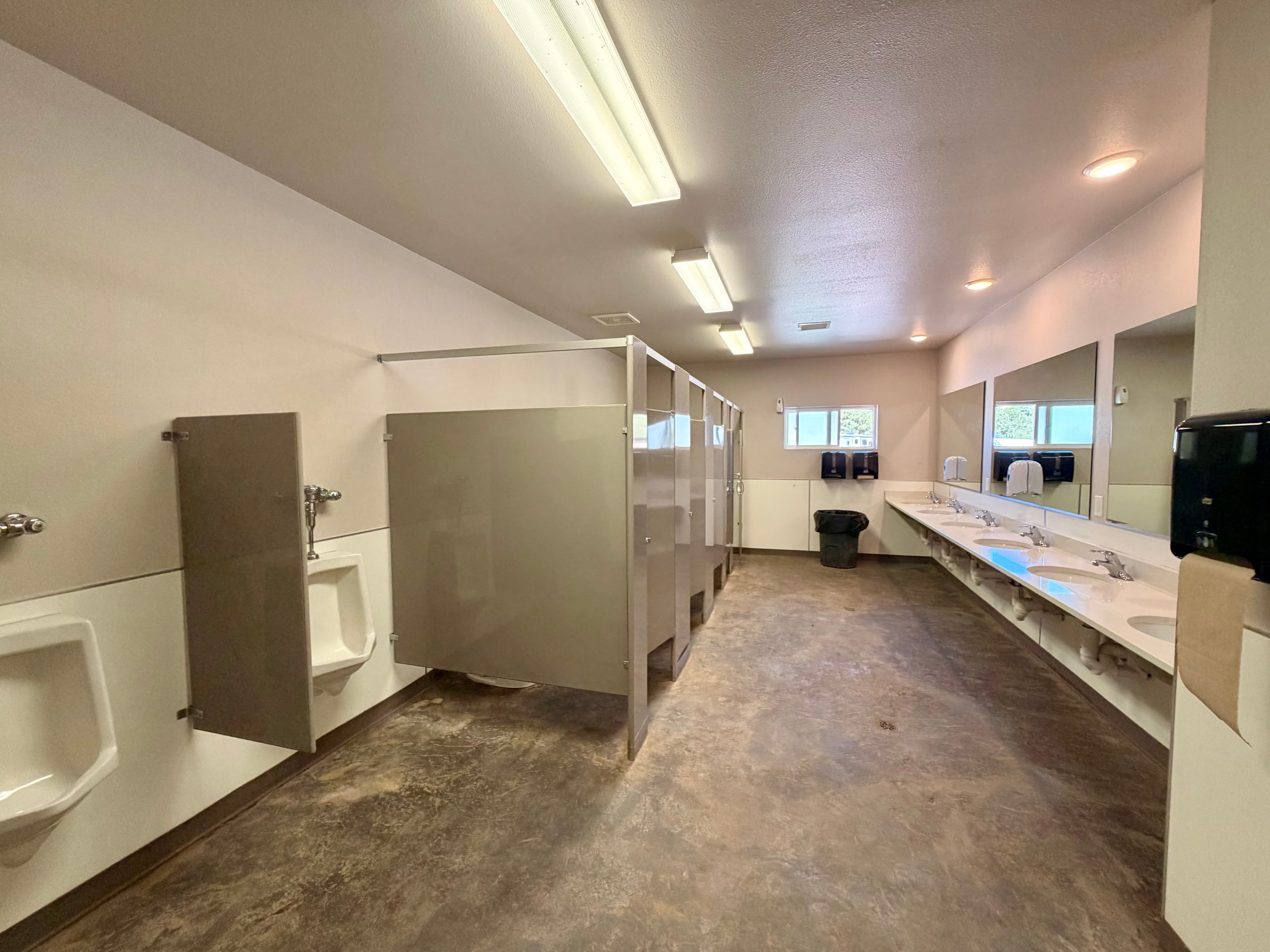 A clean, neutral-colored public bathroom with multiple stalls, urinals, and sinks.