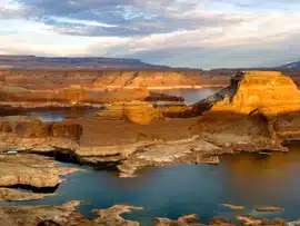 A scenic view of layered rock formations and calm water under a cloudy sky.