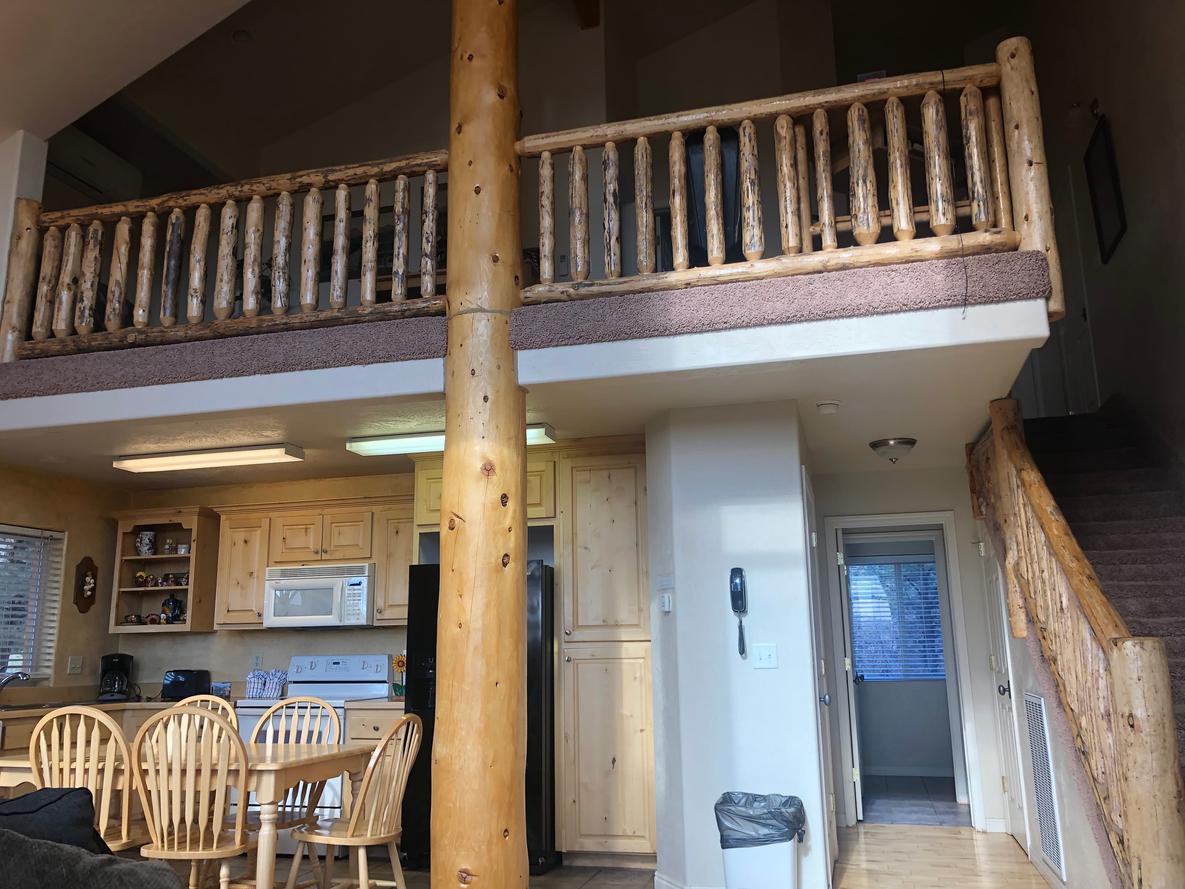A cozy kitchen and dining area with wooden furniture, featuring a staircase leading to a balcony above.