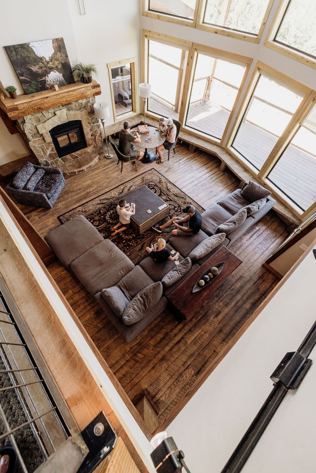 A spacious, sunlit living room with large windows, showcasing a group of people gathered around a coffee table.