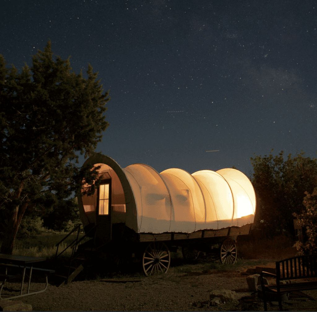 A glowing covered wagon under a starry night sky.