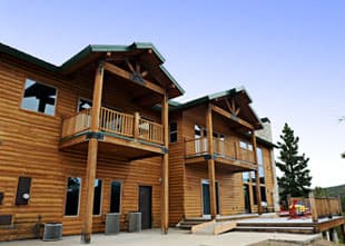A two-story wooden cabin with balconies and a clear blue sky.