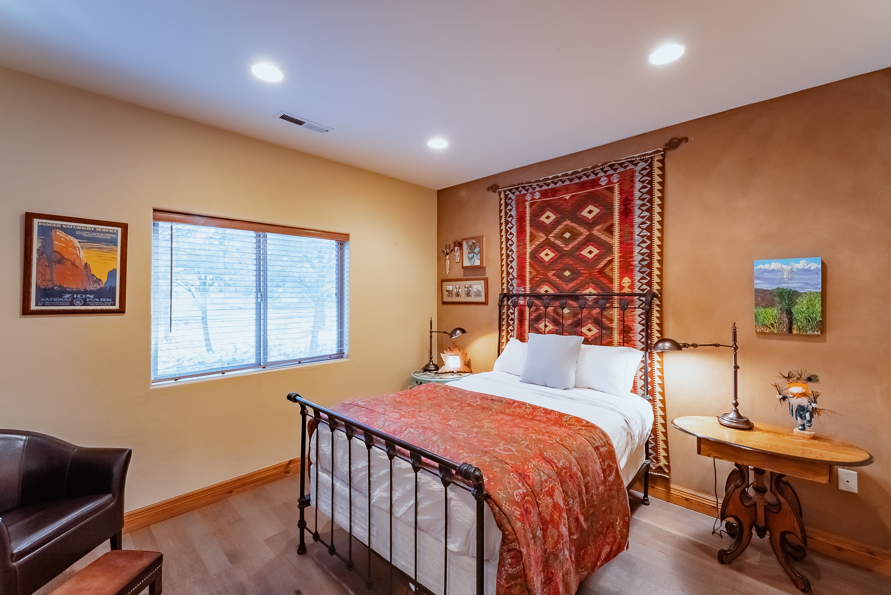 A cozy bedroom featuring a metal bed with an ornate blanket, a wooden side table, and decorative wall art.