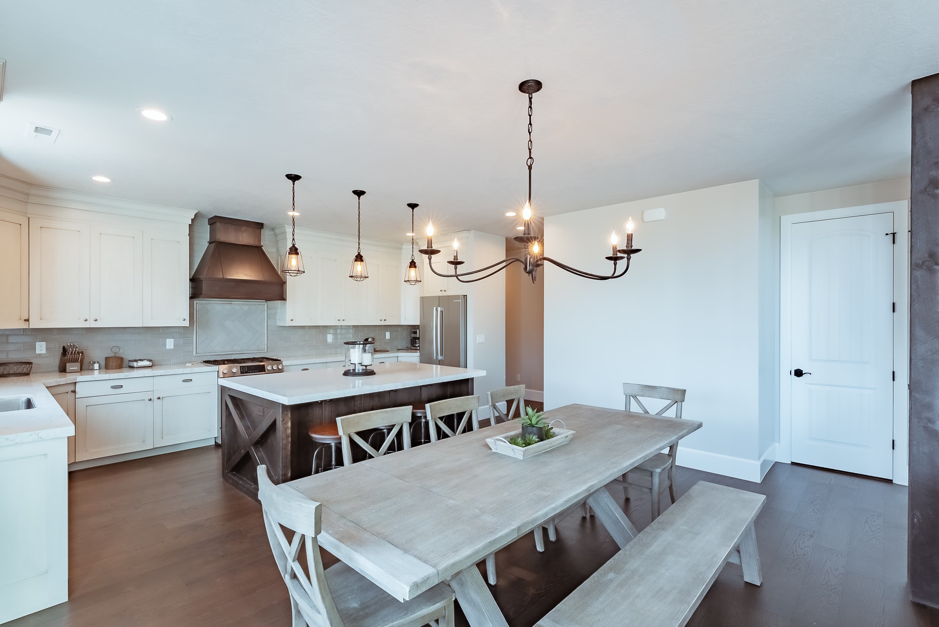 A modern kitchen and dining area featuring a large wooden table, chairs, and stylish lighting.