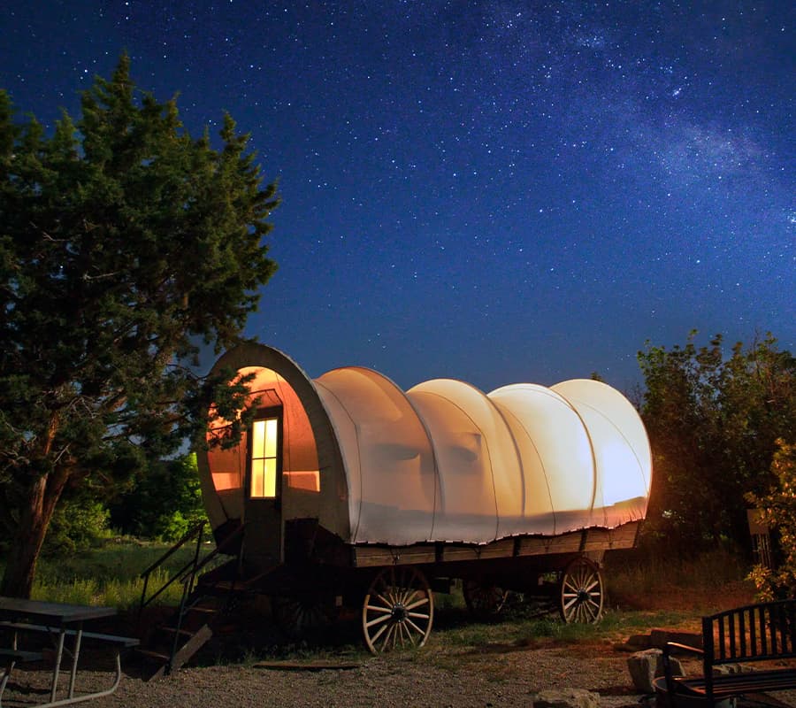 A glowing covered wagon sits under a starry night sky.