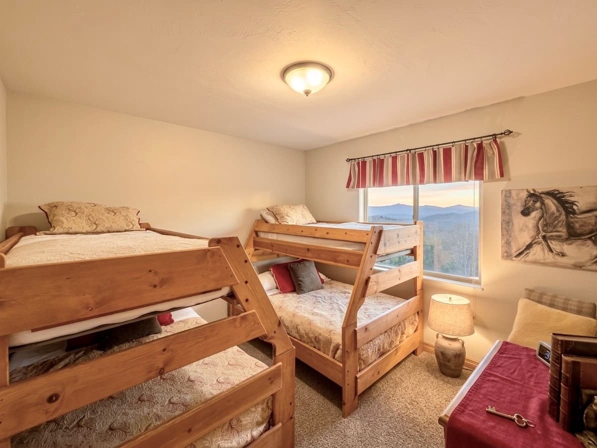A cozy bedroom featuring two sets of wooden bunk beds, a lamp, and a window with a mountain view.