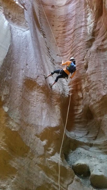 A person rappelling down a steep canyon wall.